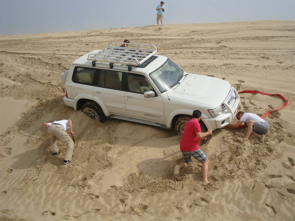 men sweeping sand from car