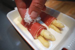 adding cheese to white asparagus wrapped in ham